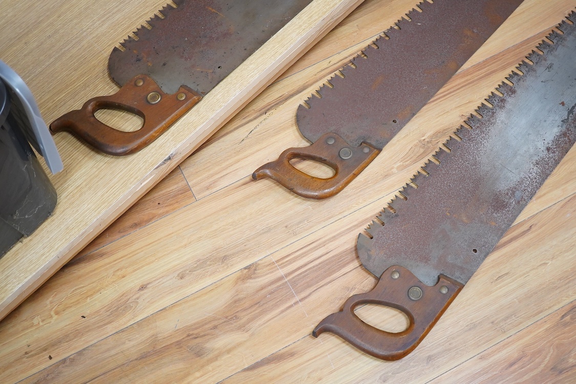 Three large Henry Disston and Sons, Philadelphia, U.S.A. early 20th century hand saws, the largest with a 5’ blade, the makers name still clear on two of the blades, all with similar style wood handles